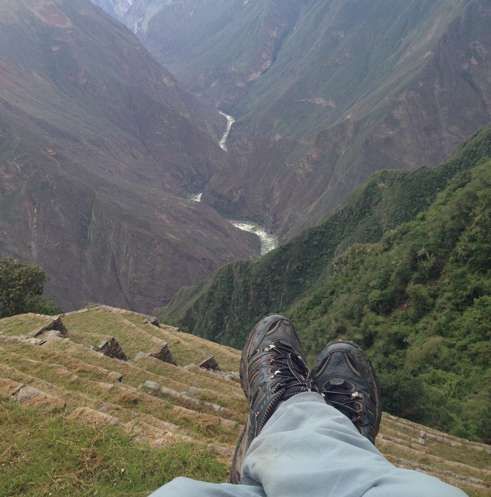 Hiker with legs crossed, sitting at choquequirao archaeological site while relaxing and viewing the massive apurimac river in the distance.